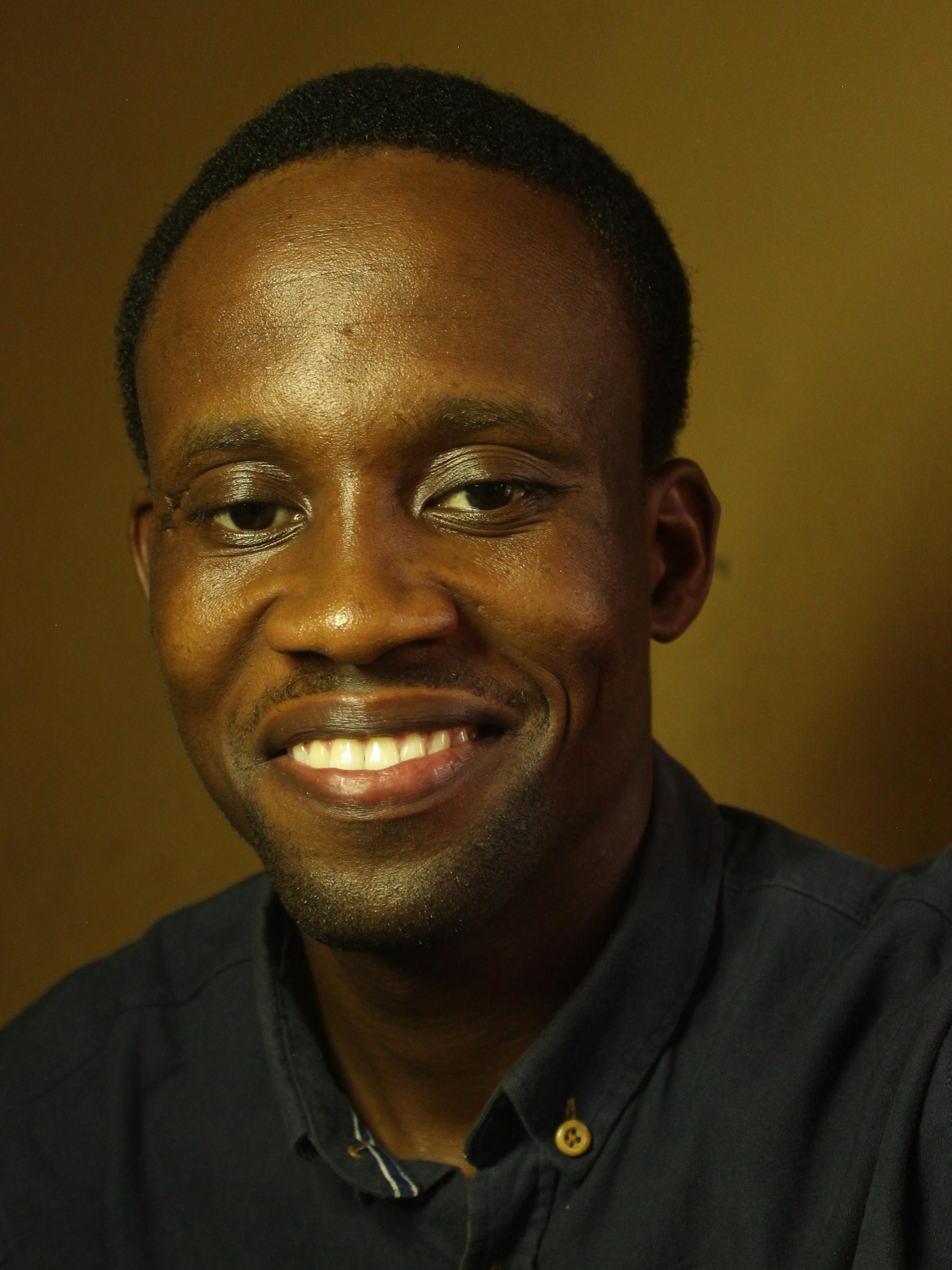 Close-up portrait of a smiling African American man in warm lighting.