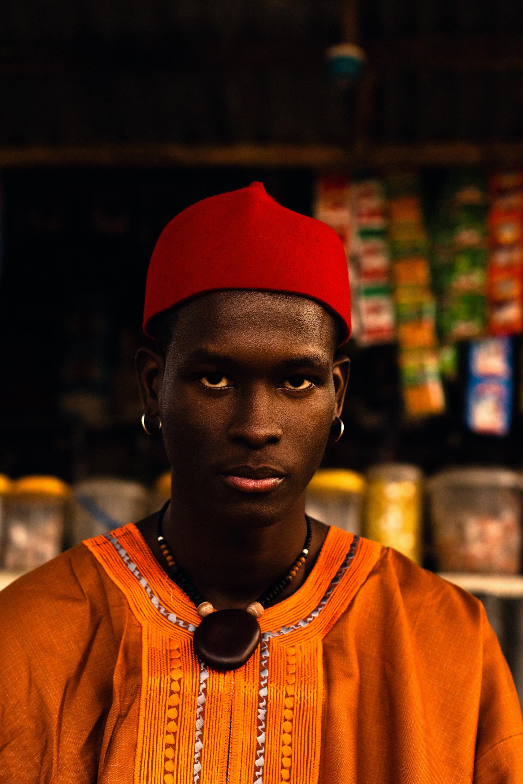 Detailed portrait of a man in traditional African clothing and red cap, showcasing cultural attire.