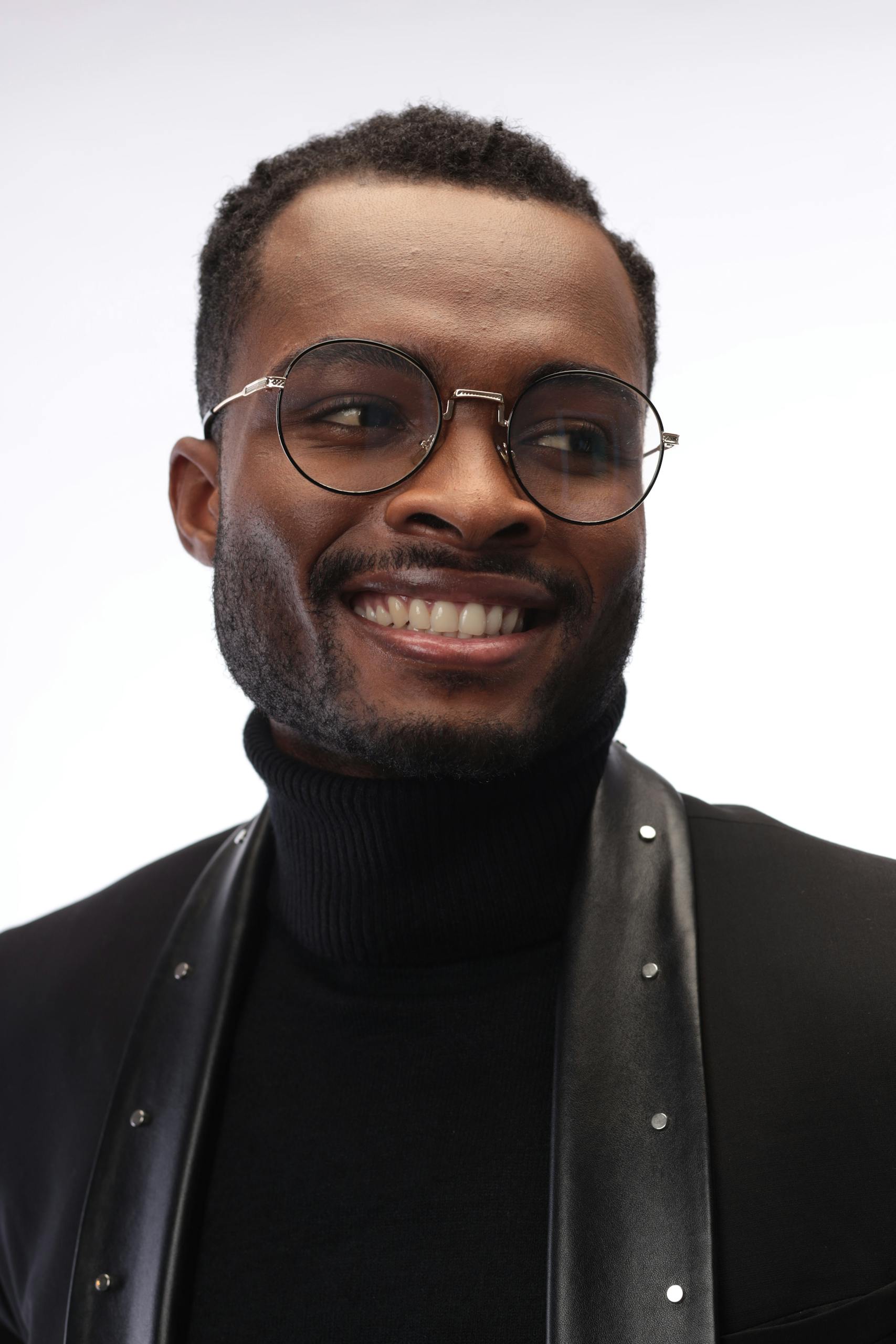 Smiling man in glasses and black attire, indoor portrait, Luanda.